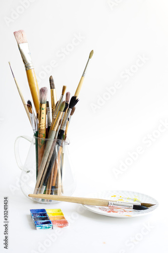 Many paint brushes stand in a glass jar. Paint brushes of different sizes and composition. Copy spase, white background