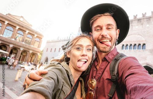 Happy boyfriend and girlfriend in love having genuine fun taking selfie at old town tour - Wanderlust life style travel vacation concept with tourist couple on city sightseeing - Bright warm filter