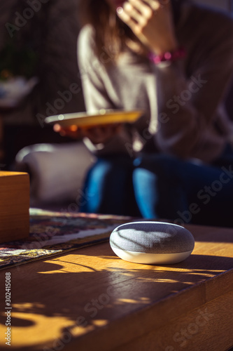 voice controlled smart speaker with a woman woman in the background in a interior home environment. Smart AI speaker concept 