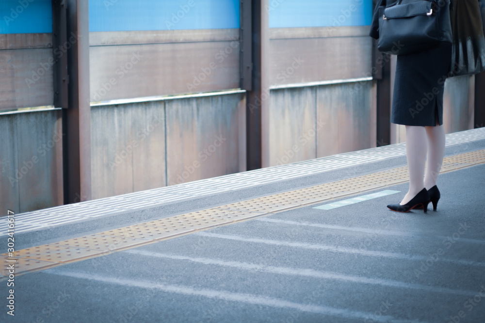 通勤・駅イメージ素材：駅のプラットフォームで電車を待つスーツ姿の女性