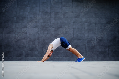 Side view of handsome fit muscular caucasian man doing inchworms exercise and looking at camera.