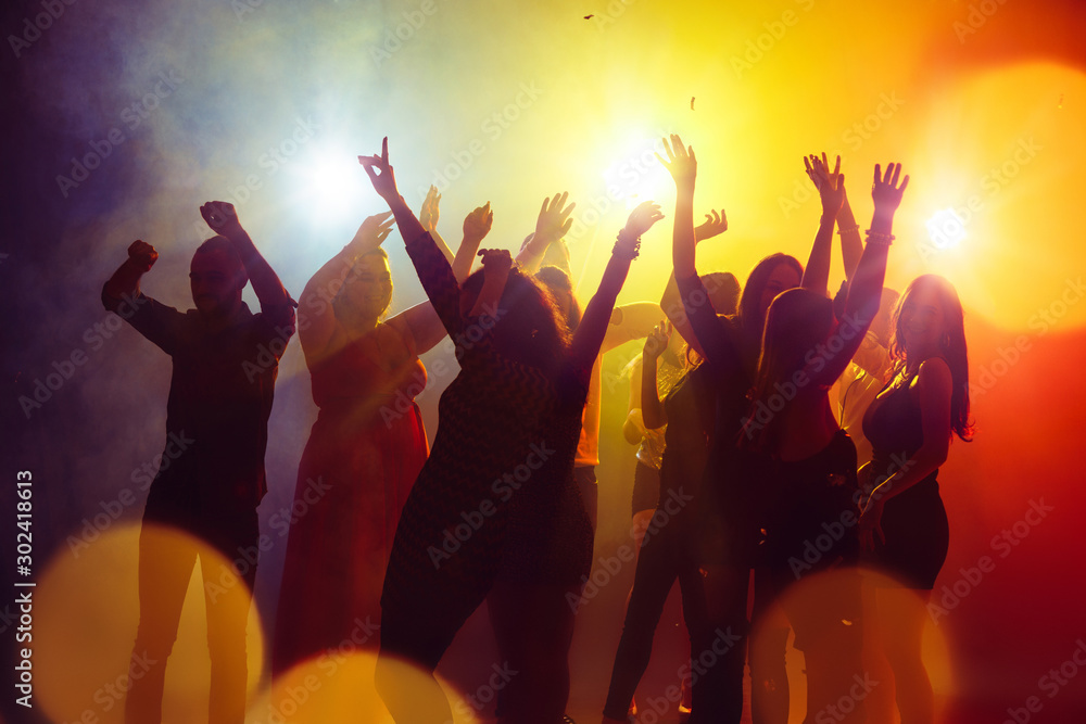 Friendship. A crowd of people in silhouette raises their hands on dancefloor on neon light background. Night life, club, music, dance, motion, youth. Yellow-blue colors and moving girls and boys. Friendship. A crowd of people in silhouette raises their hands on dancefloor on neon light background. Night life, club, music, dance, motion, youth. Yellow-blue colors and moving girls and boys.