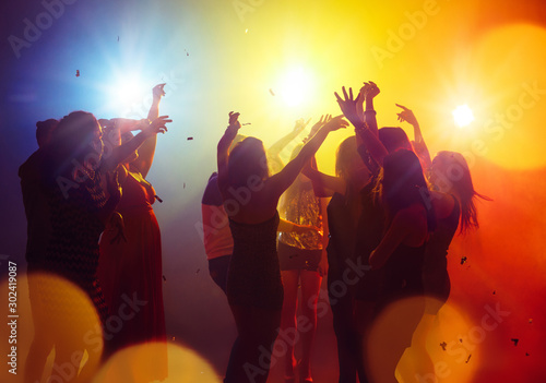 Weekend. A crowd of people in silhouette raises their hands on dancefloor on neon light background. Night life, club, music, dance, motion, youth. Yellow-blue colors and moving girls and boys.