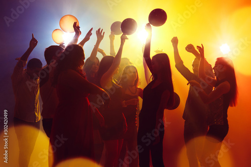Happiness. A crowd of people in silhouette raises their hands on dancefloor on neon light background. Night life, club, music, dance, motion, youth. Yellow-blue colors and moving girls and boys.
