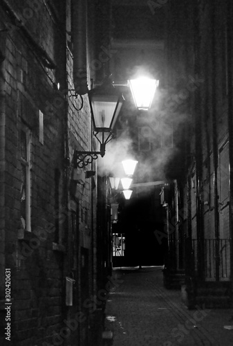 a vintage style sepia view of an old dark narrow city alley with lamplight and fog known as turks head yard in briggate leeds