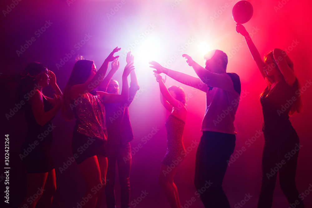 Entertainment. A crowd of people in silhouette raises their hands on dancefloor on neon light background. Night life, club, music, dance, motion, youth. Purple-pink colors and moving girls and boys.