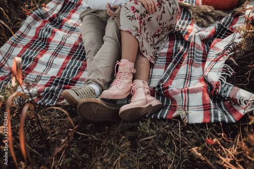 male legs in light shoes and female legs in pink boots sit on a plaid on an autumn picnic against a background of dry yellow grass