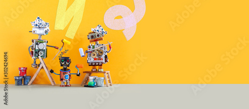 Comical robotic art. Funny toy robots house painters decorate the walls. House improvement and renovation concept. Yellow wall background, copy space