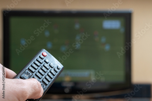 Male hand with a TV remote control close-up. Football fan watching match. Soft focus