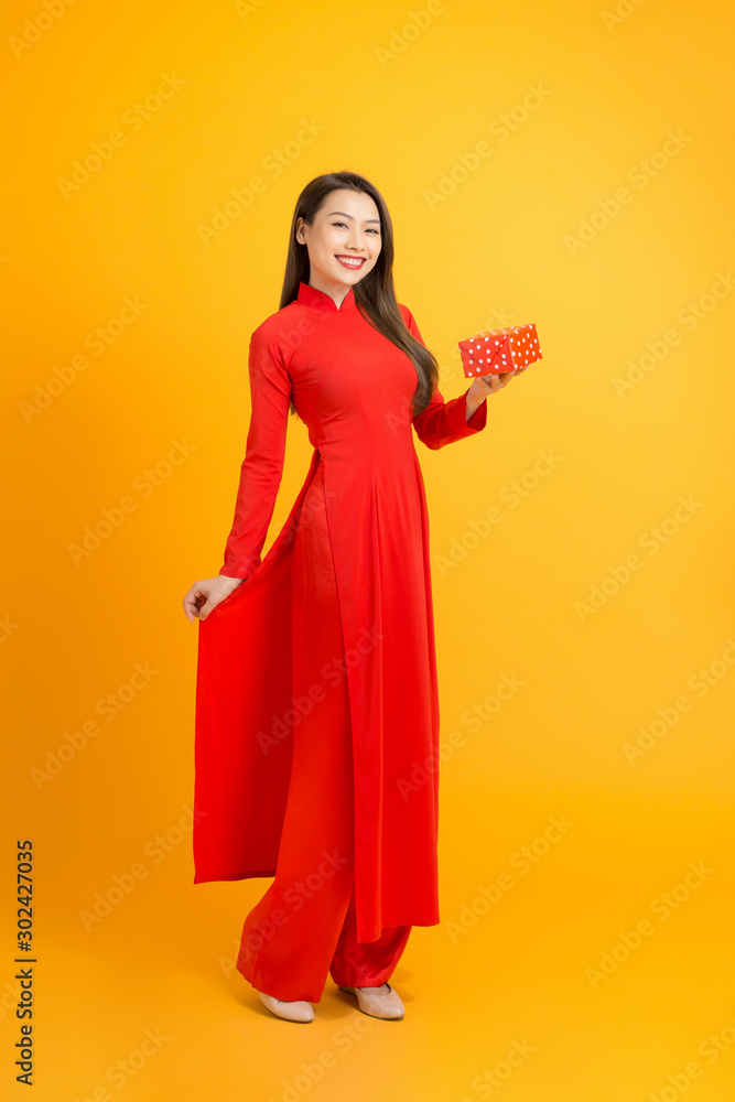 Smiling Asian woman holding gift box and wearing ao dai Vietnam. Isolated over yellow background Smiling Asian woman holding gift box and wearing ao dai Vietnam. Isolated over yellow background