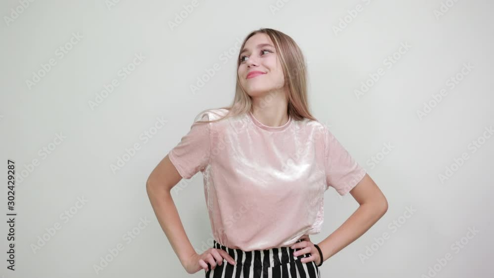 Young pretty woman wearing pastel pink shirt, keeping thumbs up on her, looking camera directly on isolated grey background raising hands Young pretty woman wearing pastel pink shirt, keeping thumbs up on her, looking camera directly on isolated grey background raising hands