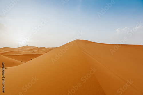 Desert landscape with orange dunes and blue sky at sunset.