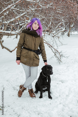 A young woman plays with her pet black Labrador outside in winter.