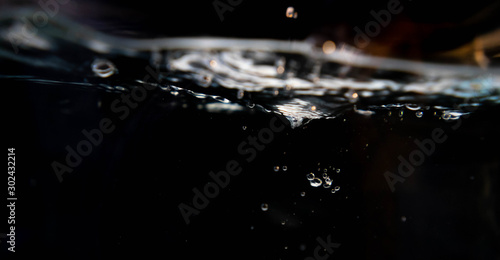 Closeup water drop and air bubbles in water in black background.