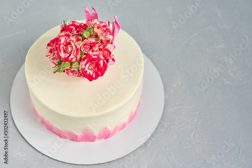 Homemade cake decorated with a crown of caramel with a natural bouquet of roses on a light concrete table.