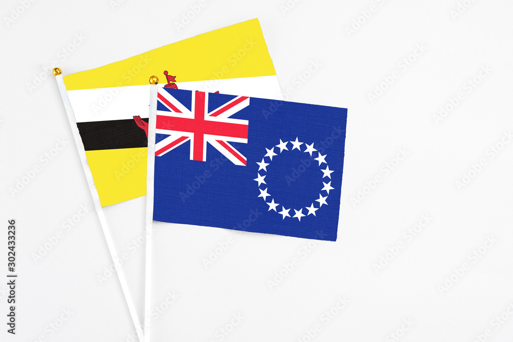Fototapeta premium Cook Islands and Brunei stick flags on white background. High quality fabric, miniature national flag. Peaceful global concept.White floor for copy space.
