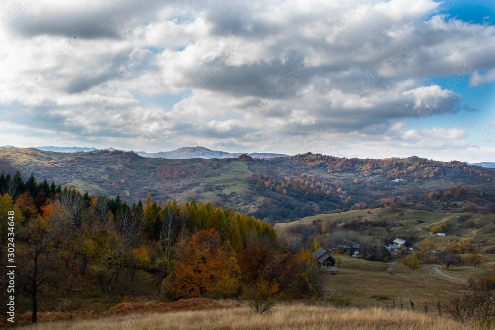 Beautiful sky and clouds over a forest on top of a hill near a small village, with autumn colored trees and autumn colors