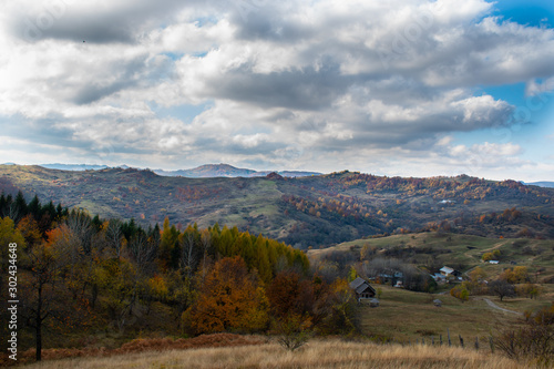 Beautiful sky and clouds over a forest on top of a hill near a small village, with autumn colored trees and autumn colors