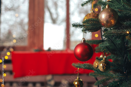 Red bauble hanging on Christmas tree. Blurry home interior background. Ball, light bokeh, New Year, celebration, holiday, copy space