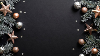 Christmas frame. Black Xmas background with pine tree branches, copper color stars, balls, confetti. Christmas frame, greeting card template, web banner mockup. Flat lay, top view, copy space