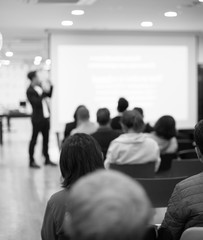 Speaker on the stage with rear view of audience in the conference hall or seminar meeting, business and education concept. Speaker giving a talk at business meeting. Seminar presentation photo.