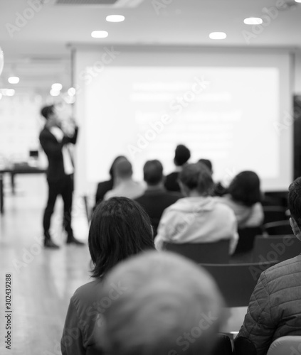 Speaker on the stage with rear view of audience in the conference hall or seminar meeting, business and education concept. Speaker giving a talk at business meeting. Seminar presentation photo.