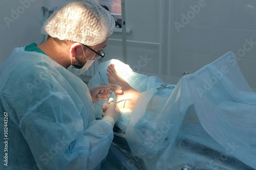 Wallpaper Mural Surgeon man sutures ankle during surgery with neat stitches after removing hygroma. Doctor sewing on wound in operating room in hospital. Seams with self-absorbable threads. One day surgery concept. Torontodigital.ca