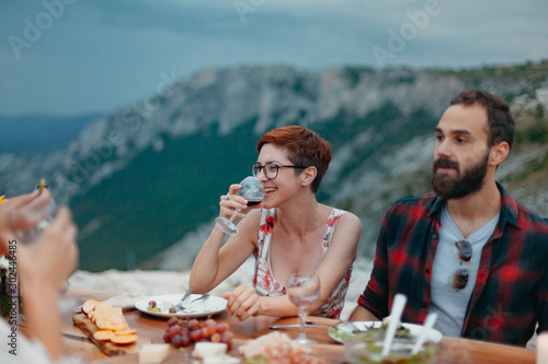 Friends and family gathered for picnic dinner for Thanksgiving. Festive young people celebrating life with red wine, grapes, cheese platter, and a selection of cold meats