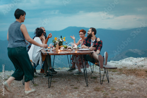 Friends and family gathered for picnic dinner for Thanksgiving. Festive young people celebrating life with red wine, grapes, cheese platter, and a selection of cold meats © Suteren Studio