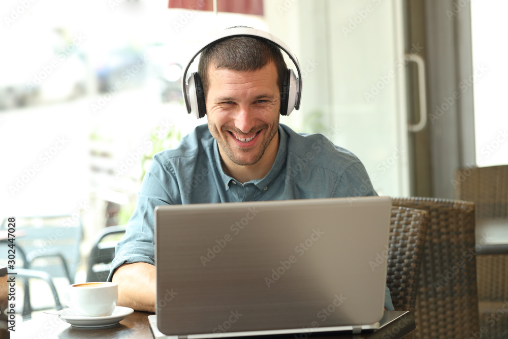 Happy man using a laptop with headphones in a bar Happy man using a laptop with headphones in a bar