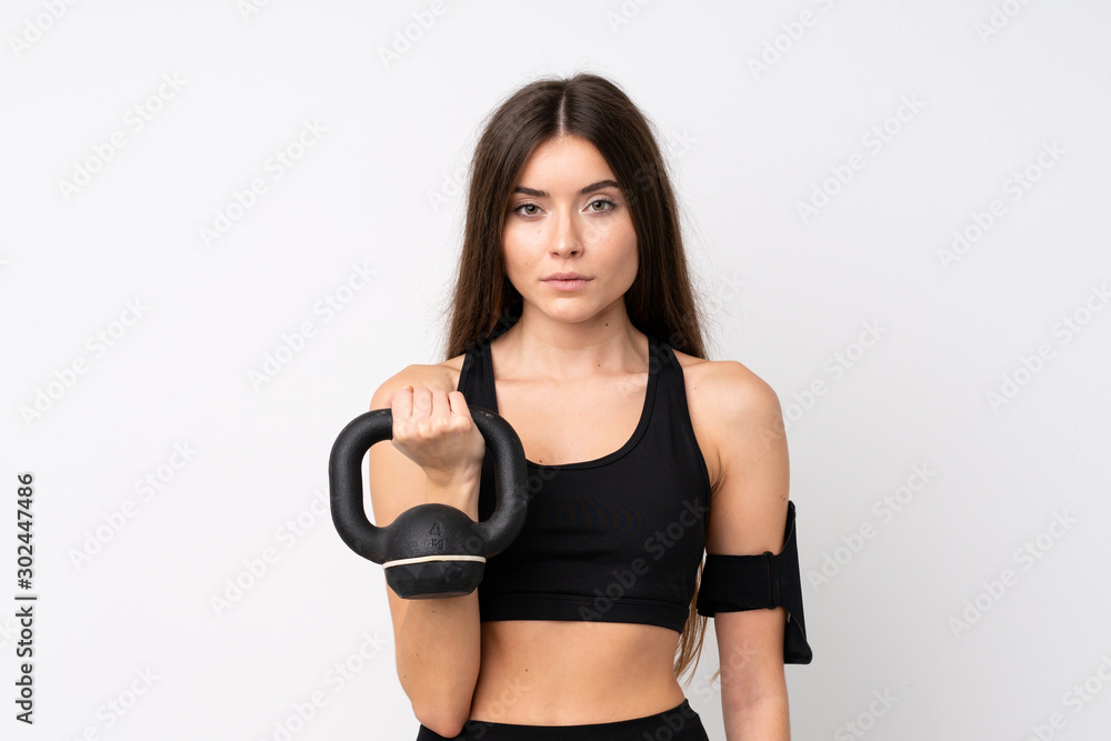 Fototapeta premium Young sport woman over isolated white background making weightlifting with kettlebell and looking to the front