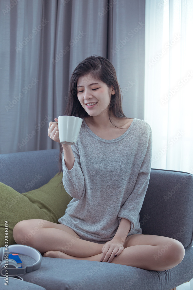 A beautiful woman with a cup of coffee to sit on the sofa with the light on the window A beautiful woman with a cup of coffee to sit on the sofa with the light on the window