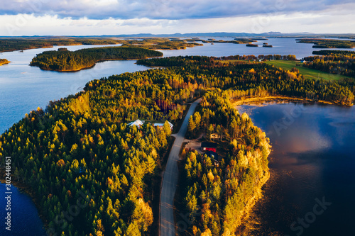 Aerial view of road through autumn forest with blue lakes in Finland.
