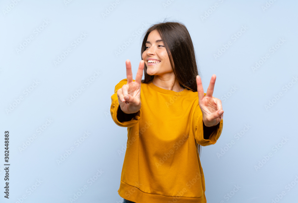 Caucasian young woman over isolated blue wall smiling and showing victory sign Caucasian young woman over isolated blue wall smiling and showing victory sign