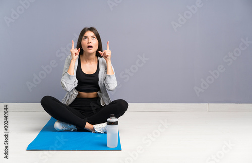 Young sport woman sitting on the floor with mat pointing with the index finger a great idea