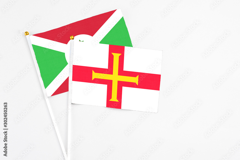 Fototapeta premium Guernsey and Burundi stick flags on white background. High quality fabric, miniature national flag. Peaceful global concept.White floor for copy space.