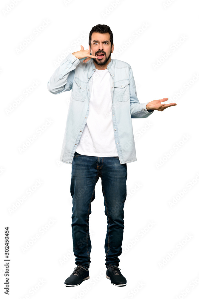 Fototapeta premium Full-length shot of Handsome man with beard making phone gesture and doubting over isolated white background
