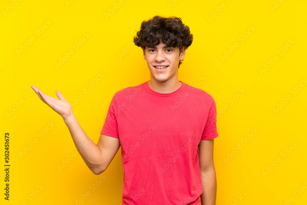 Young man over isolated yellow wall holding copyspace imaginary on the palm Young man over isolated yellow wall holding copyspace imaginary on the palm