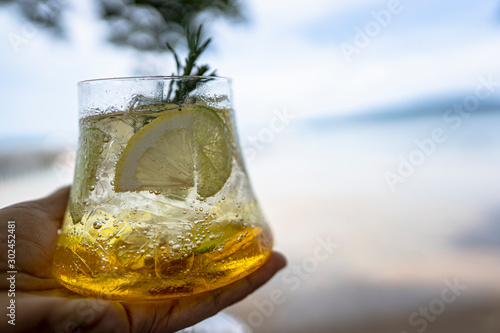 hand holding sparkling lemonade soda with blurry beach background