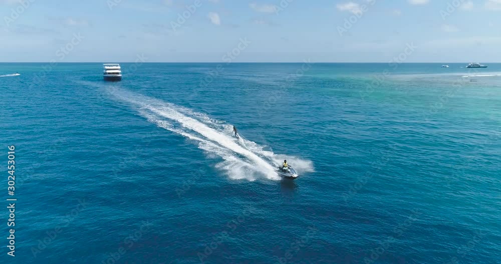 Drone tracking shot Over Man Riding A Jet Ski At Tropical Paradise Exotic Island with blue and turquoise ocean sea view. Adventure Concept for Tourist Attraction at Beach Vacation sport at Summer day