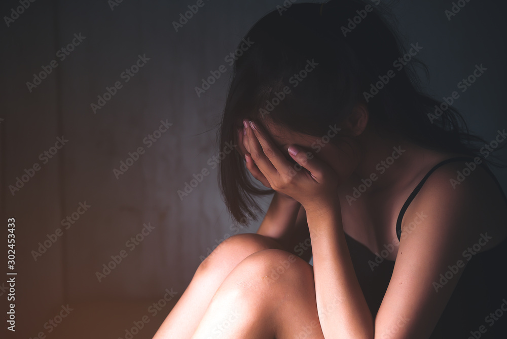 Naklejka premium Sad depressed woman suffering from family life. women sitting in dark room cryng, palm close her face. Young beautiful women thinking how to solve problem.
