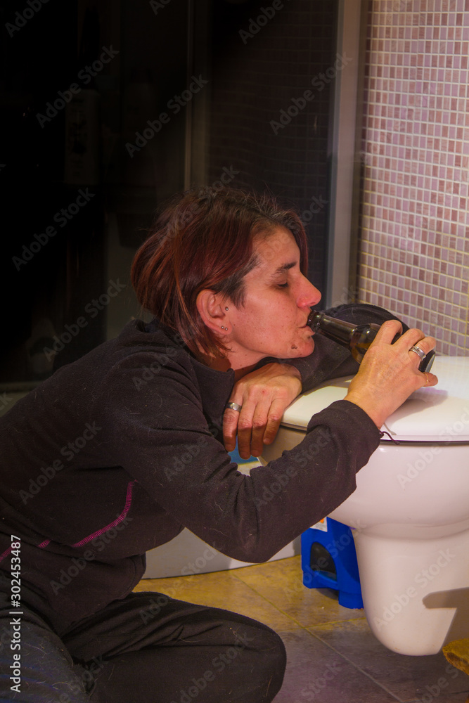 drunk girl drinking from the bottle in the bathroom lying on the ground  Stock Photo | Adobe Stock