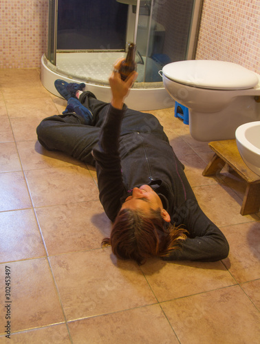 drunk girl drinking from the bottle in the bathroom lying on the ground © Mirko