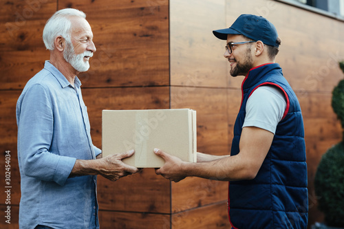 Bilde på lerret Young smiling courier delivering package to a senior customer.