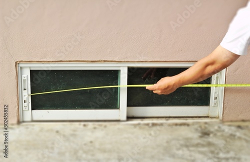 Measuring length of sliding glass window, basement, tape measure, yellow line Inspect window installation, house construction, home builder, inspect house