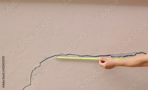 The builders use the yellow tape measure to measure the cracks on the brown wall. Before repair Cracks in the walls from the subsidence of house structures