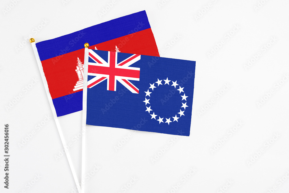 Fototapeta premium Cook Islands and Cambodia stick flags on white background. High quality fabric, miniature national flag. Peaceful global concept.White floor for copy space.