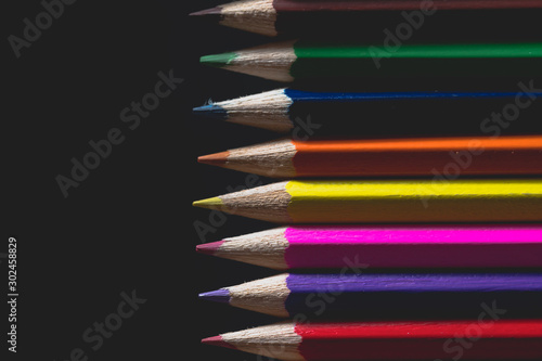 Coloured pencils isolated on black background close up. Vintage look Macro photography. Pencils Wallpaper. Bundle of rainbow colored pencils with selected focus on tips. Multicolored rainbow pencils.