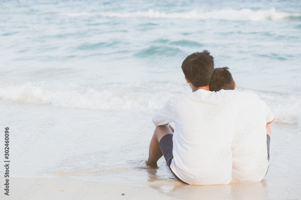 Back view homosexual portrait young asian couple sitting hug together on beach in summer, asia gay going tourism for leisure and relax with romantic and happy in vacation at sea, LGBT legal concept.