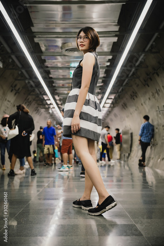 Portrait of Asian young short hair beautiful woman wearing glasses and grey dress standing turn back posing in the crowd in tunnel
